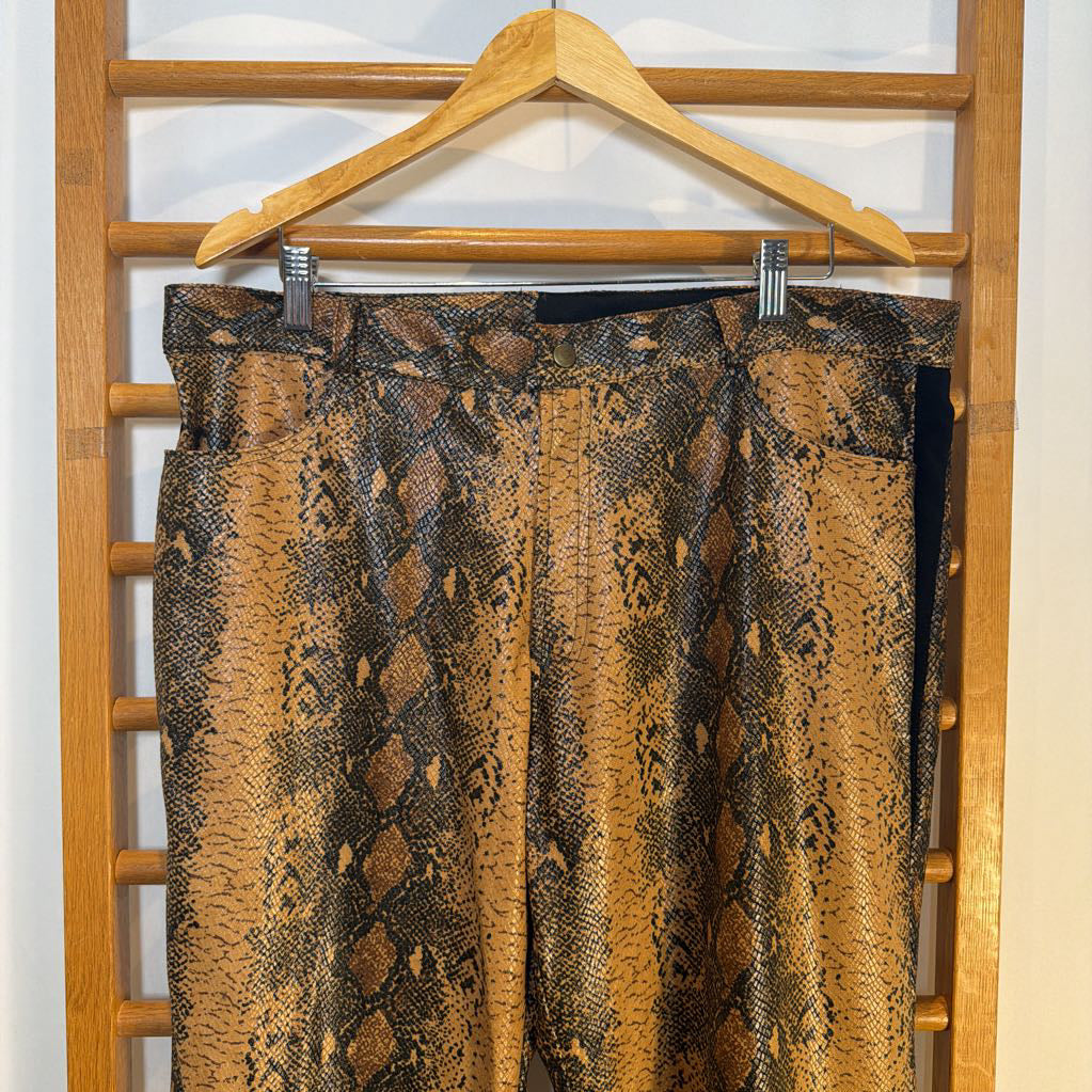 Snakeskin-patterned pants on a wooden hanger against a white wall.