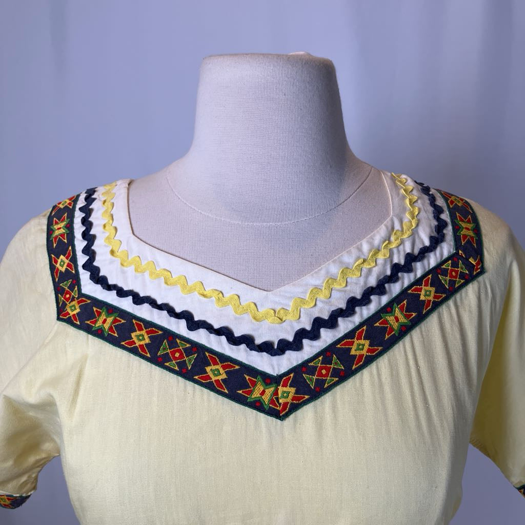 Mannequin wearing a cream-colored top with colorful embroidered neckline against a light purple background