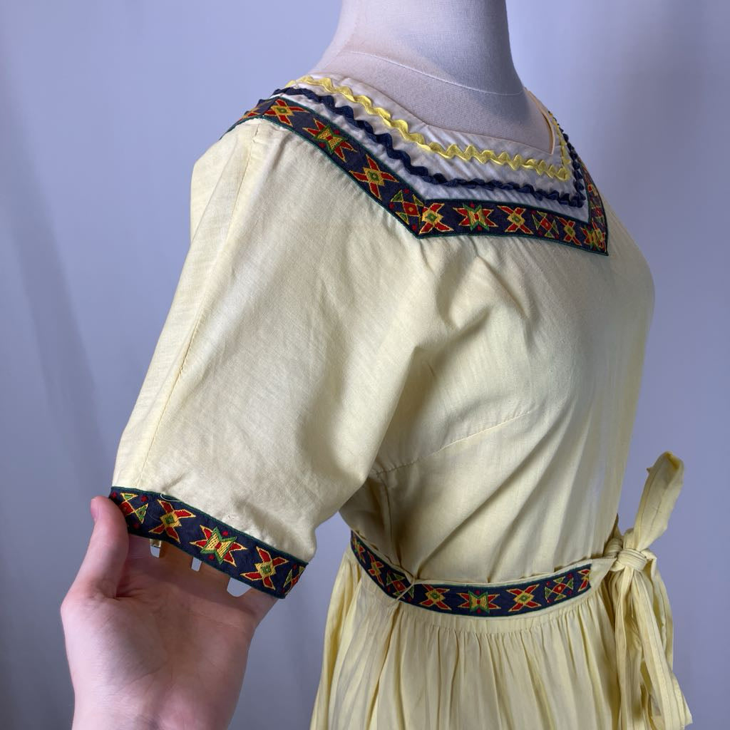 Mannequin wearing a light yellow dress with colorful embroidery on a plain background