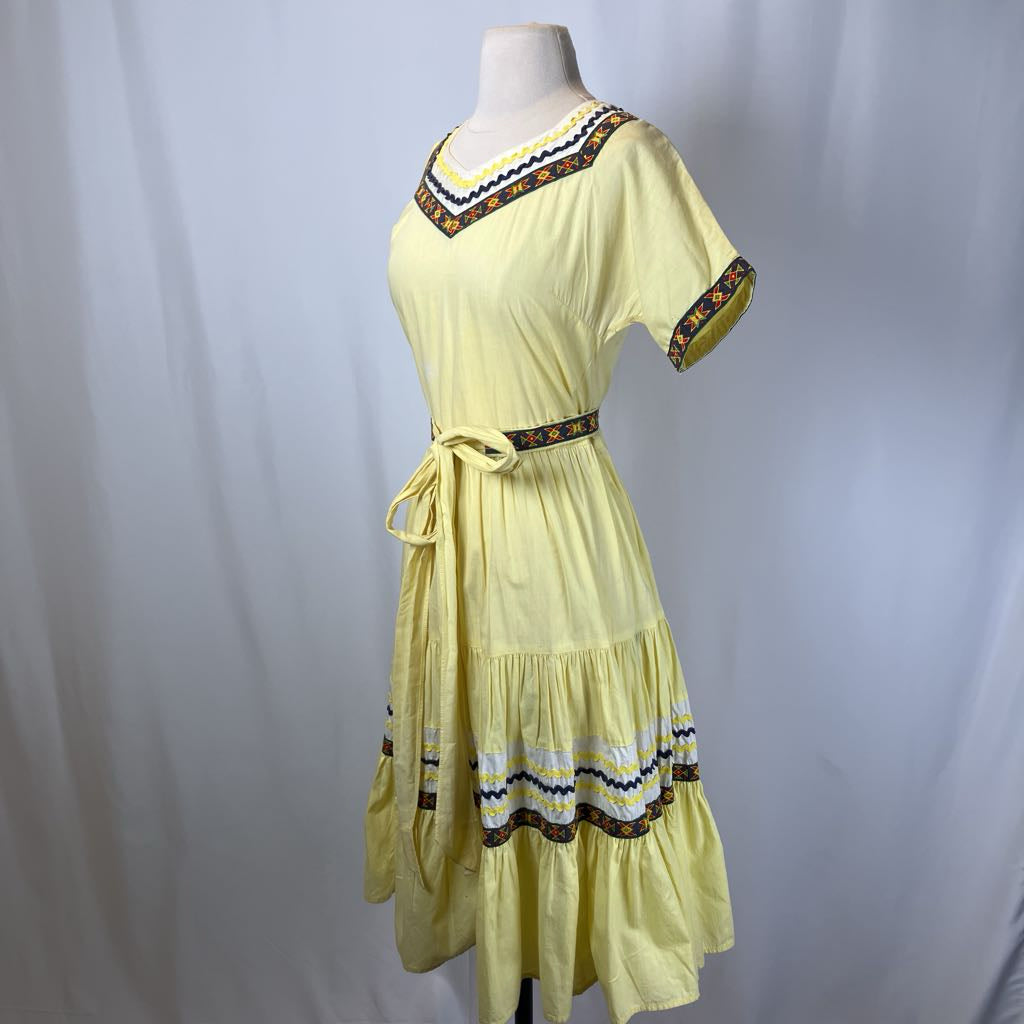 Yellow dress with decorative trim on a mannequin against a plain background