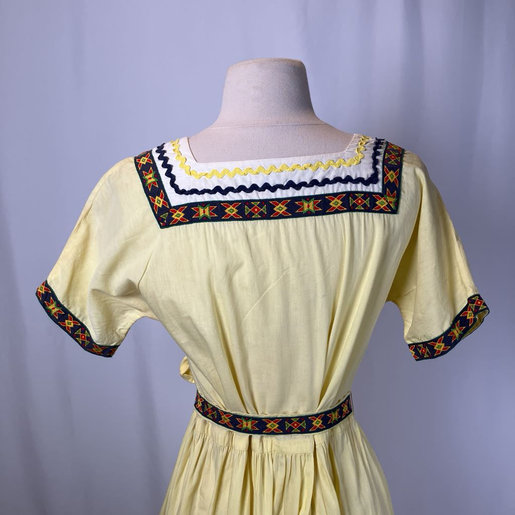 Yellow dress with embroidered details on a mannequin against a plain background