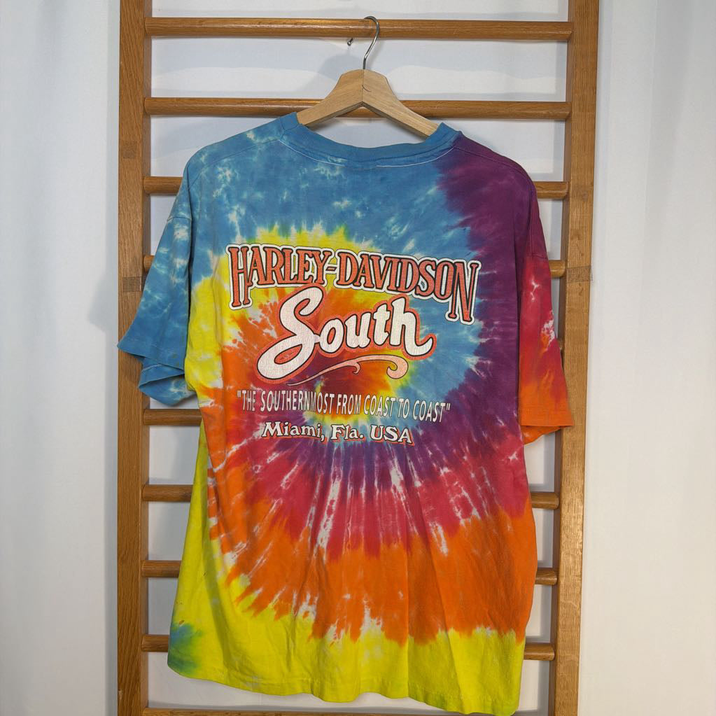 Colorful tie-dye Harley-Davidson shirt on a hanger against a wooden ladder background.