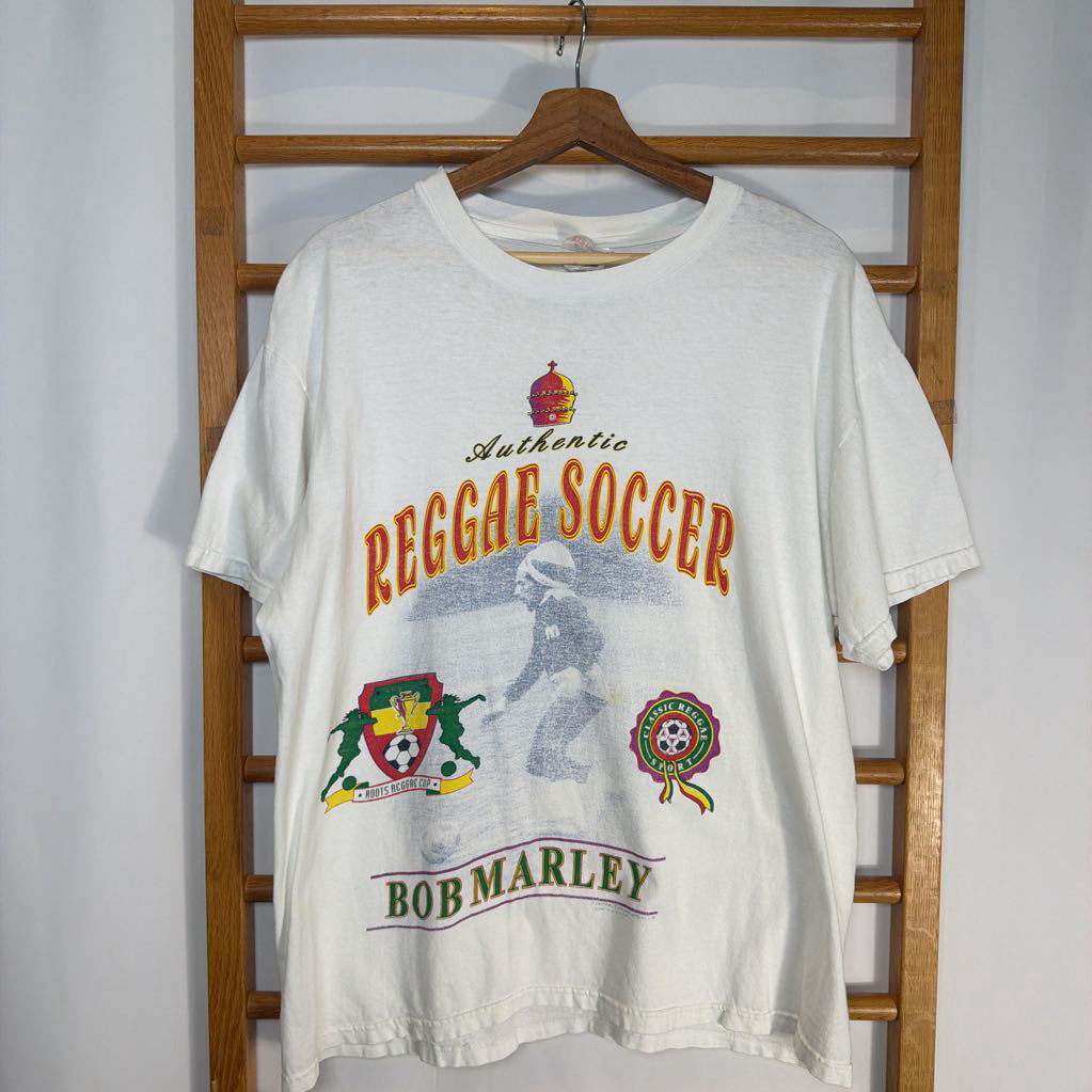 White t-shirt with 'Reggae Soccer Bob Marley' design on a wooden rack.