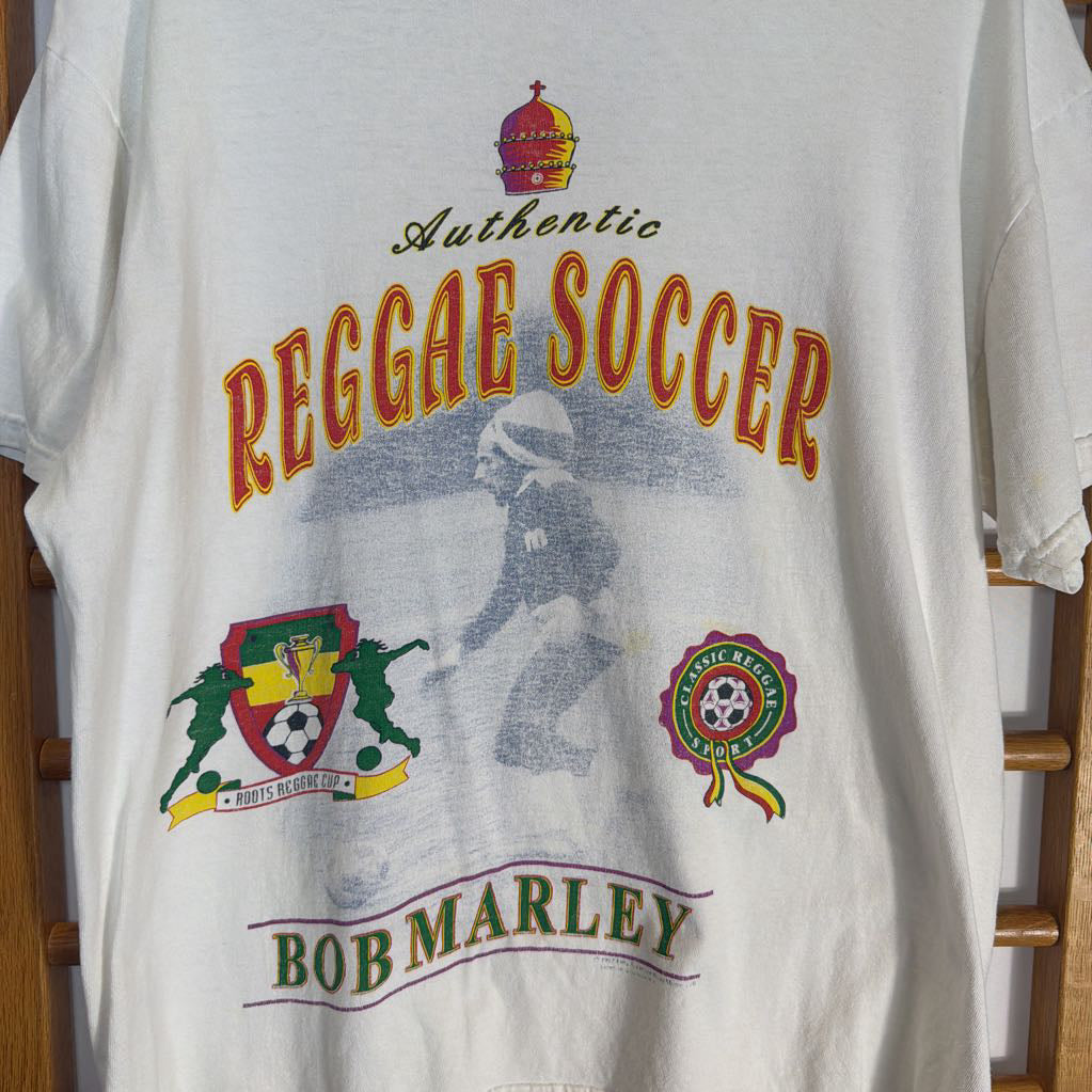 White t-shirt with 'Authentic Reggae Soccer Bob Marley' design on a wooden rack.