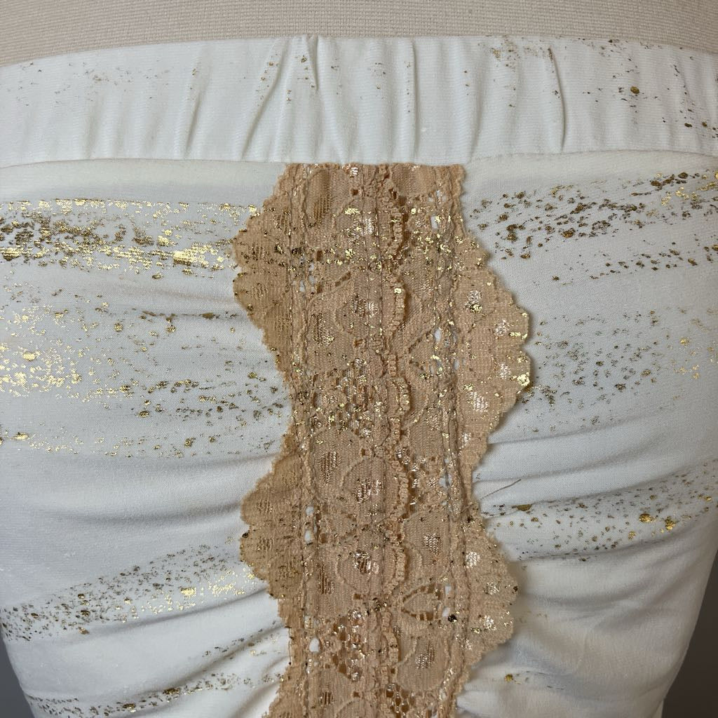Close-up of a beige lace trim on a white fabric background with gold sequins.