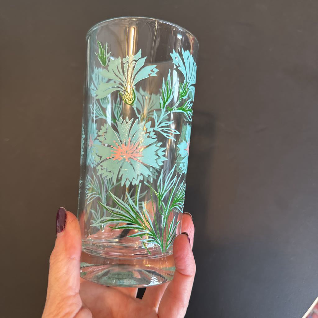 Clear glass tumbler with floral etching held by a hand against a dark background