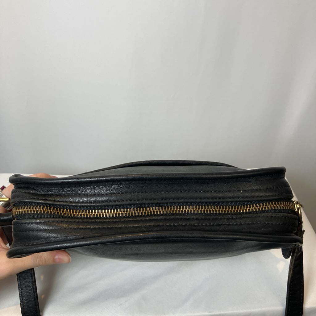 Black leather bag with gold zipper held against a plain background