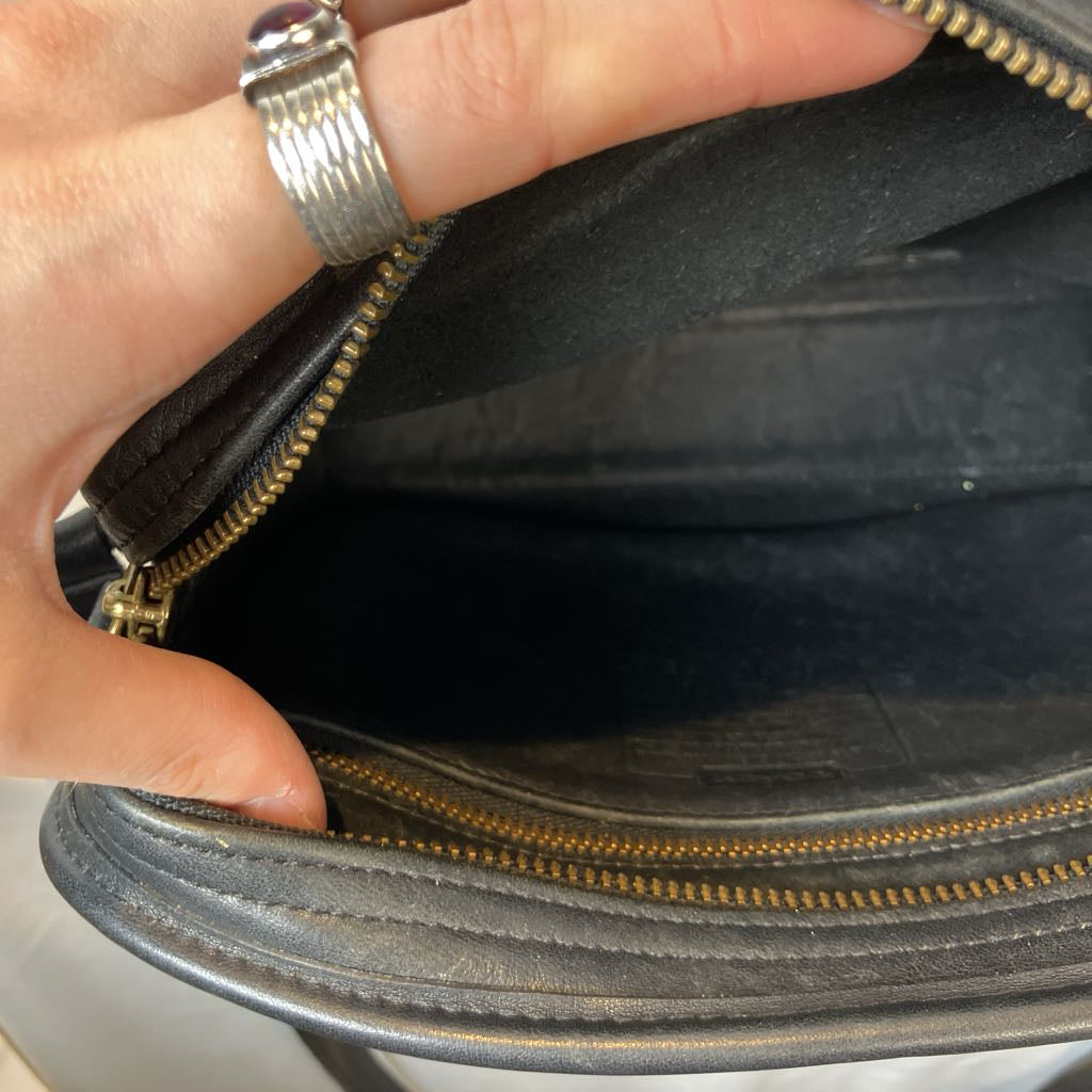 Hand opening a black leather handbag with gold zipper