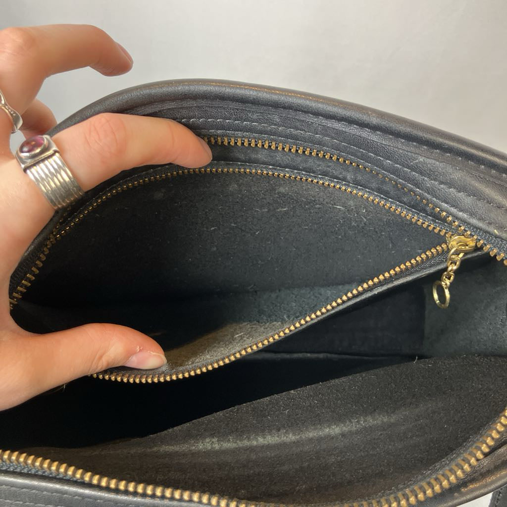 Hand holding a black leather bag with gold zipper