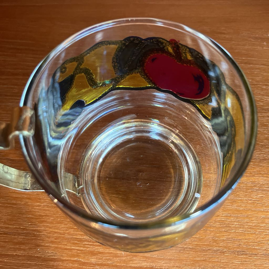 Clear glass mug with a decorative handle featuring a fruit design on a wooden surface