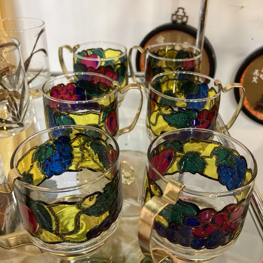 Set of glass mugs with colorful floral designs on a reflective surface.