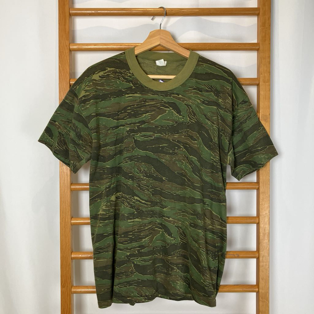 Green camouflage t-shirt on a wooden hanger against a white wall