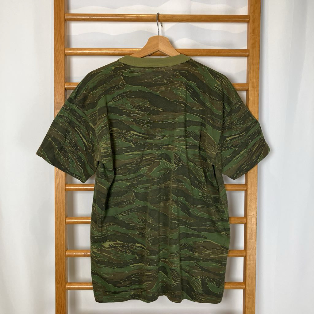 Green camouflage shirt on a hanger against a wooden rack.