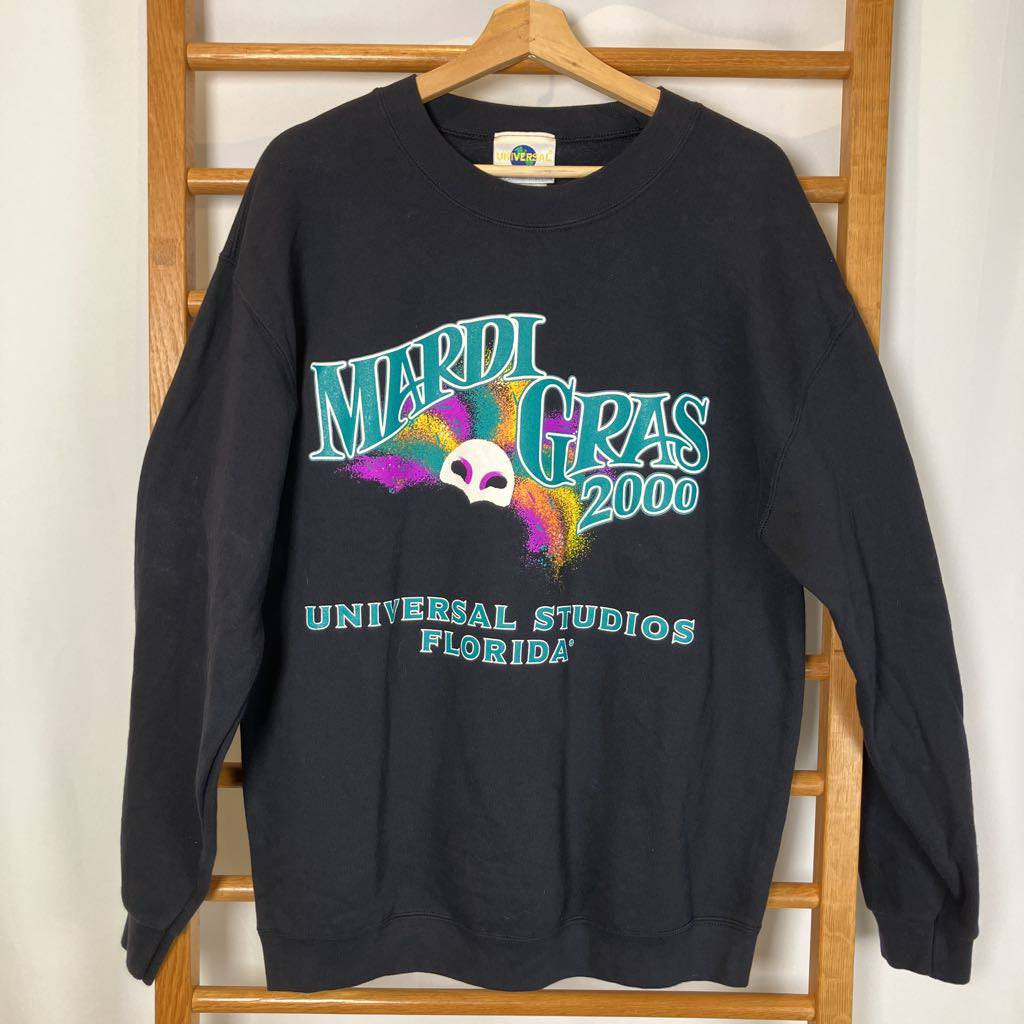Black sweatshirt with Mardi Gras 2000 design on a wooden hanger against a white wall