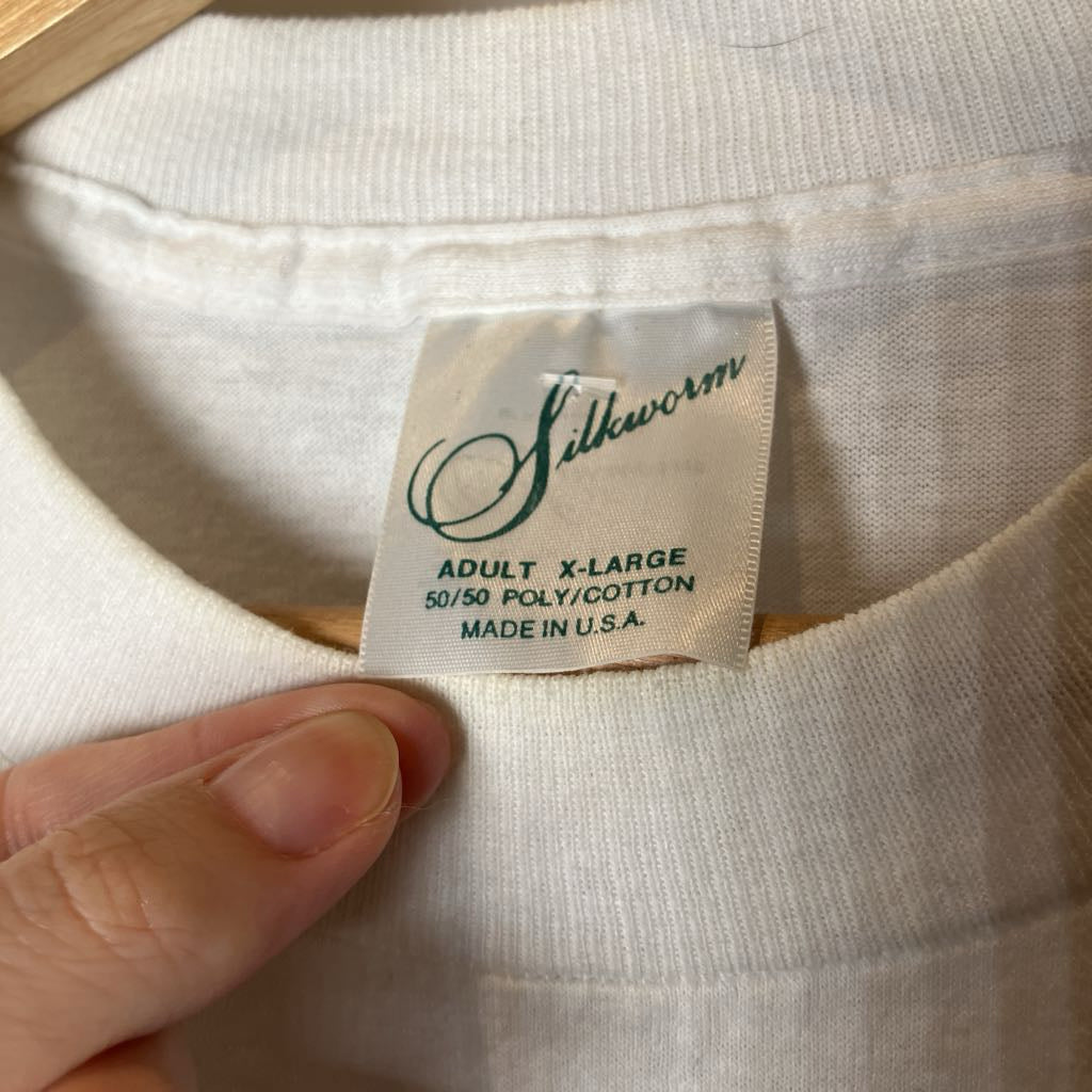 Close-up of a white t-shirt neck label reading 'Silkworm' with size details, held by a hand.