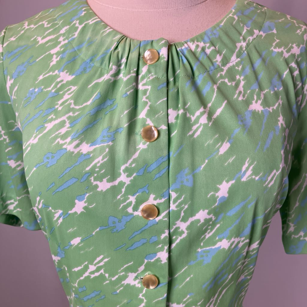 Green dress with abstract pattern and gold buttons on a mannequin against a purple background
