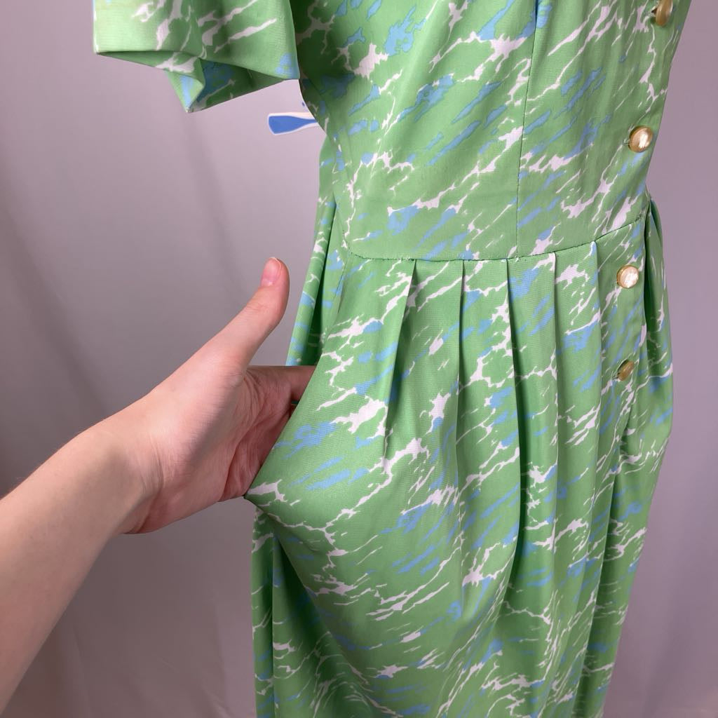 Green dress with abstract pattern held by a hand against a gray background