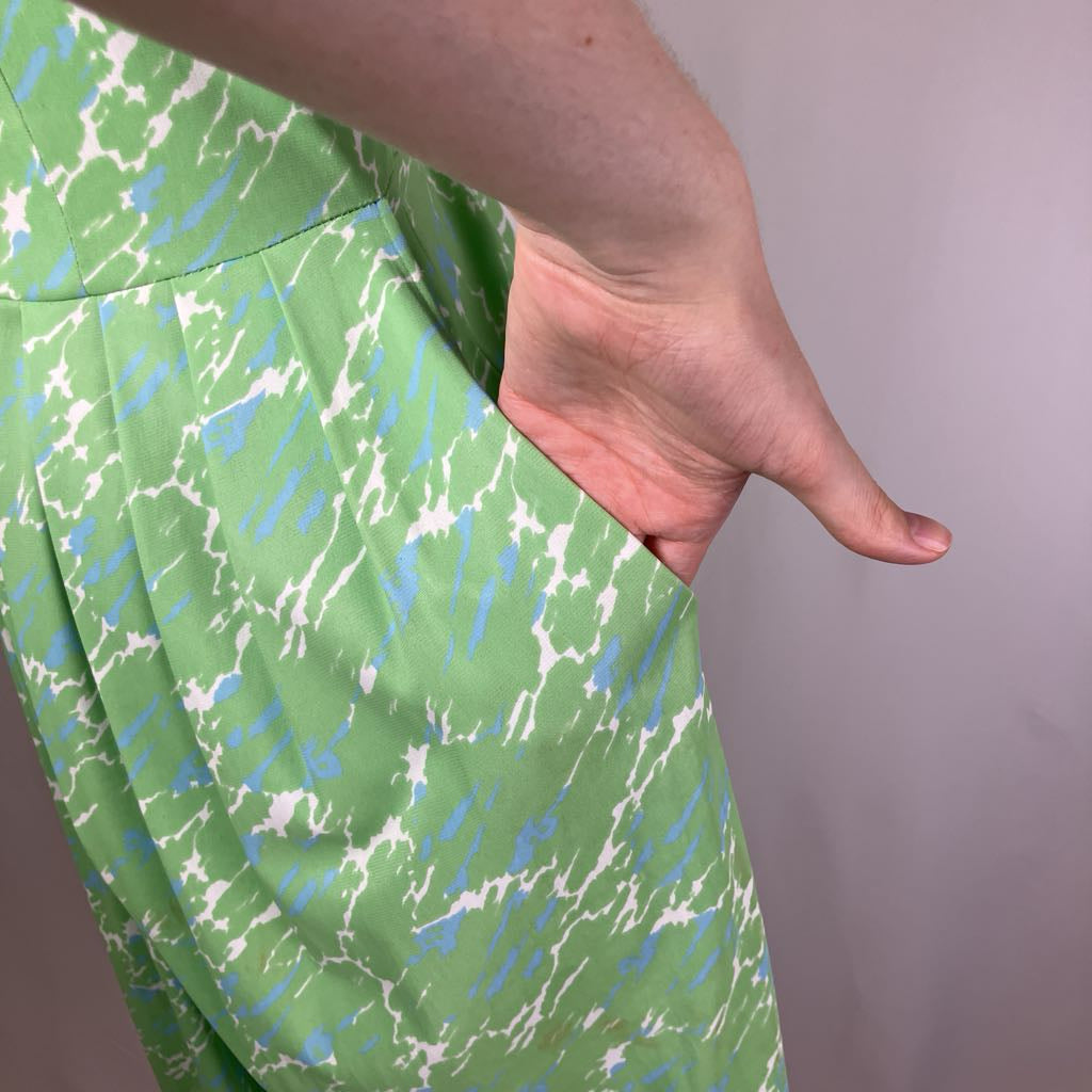 Green fabric with blue and white pattern held by a hand against a plain background