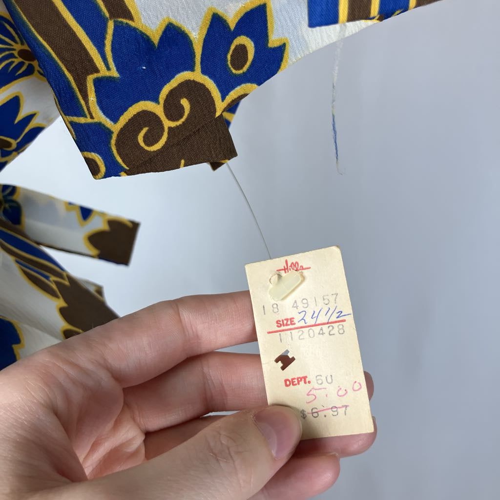 Hand holding a vintage clothing tag with text on a patterned fabric background
