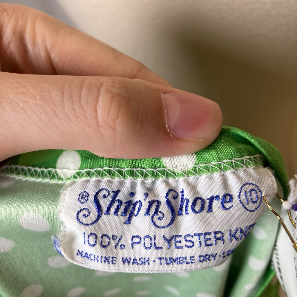 Close-up of a 'Ship'n Shore' label on green fabric with white polka dots.