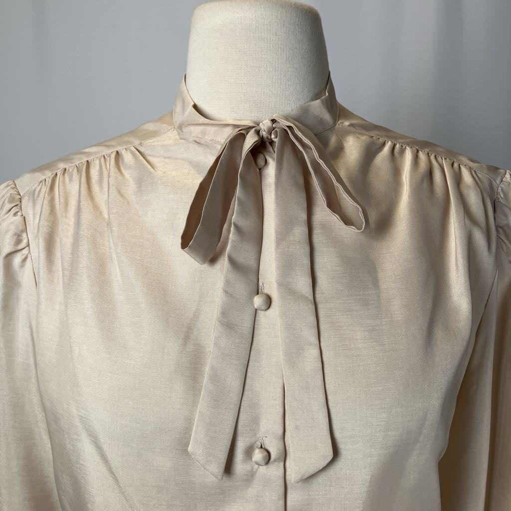 Beige blouse with a tie collar on a mannequin against a gray background