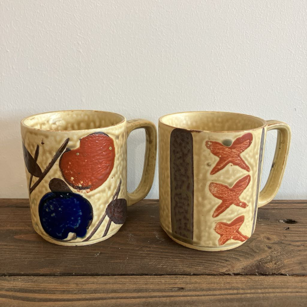 Two ceramic mugs with decorative designs on a wooden surface.