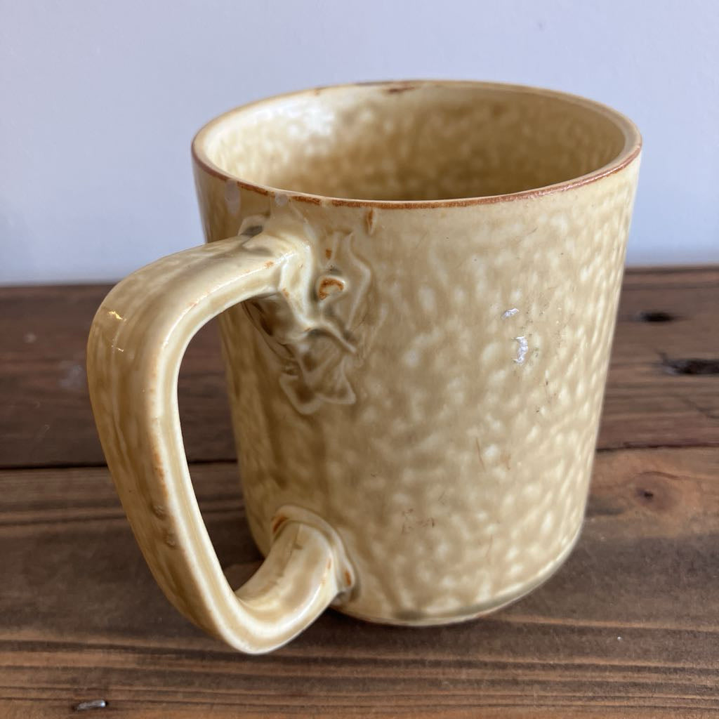 Beige ceramic mug with textured surface on a wooden surface