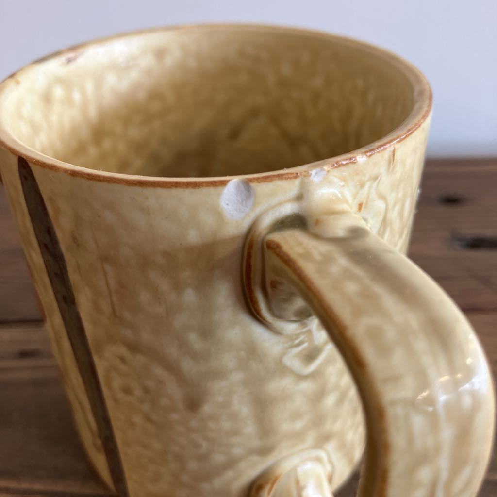 Close-up of a beige ceramic mug with a textured surface on a wooden surface.