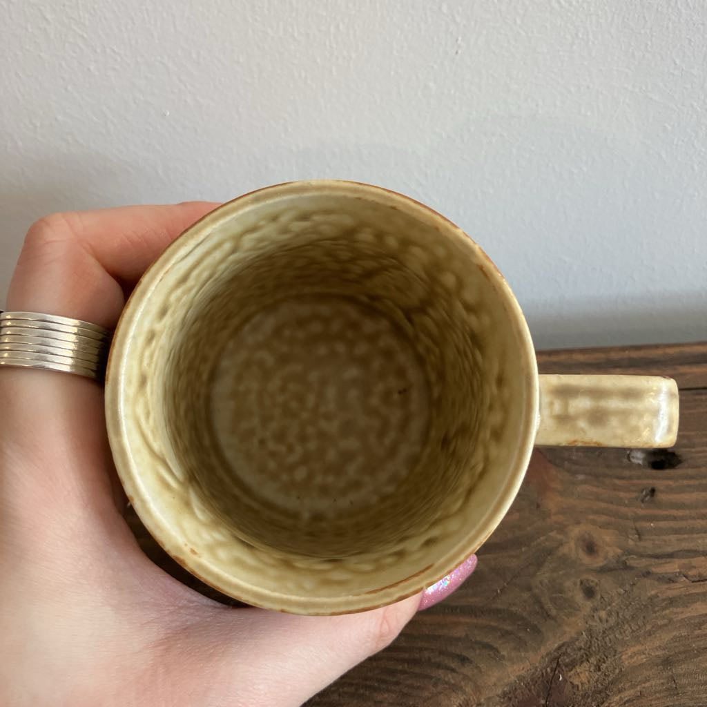 Hand holding a textured ceramic mug on a wooden surface with a white background