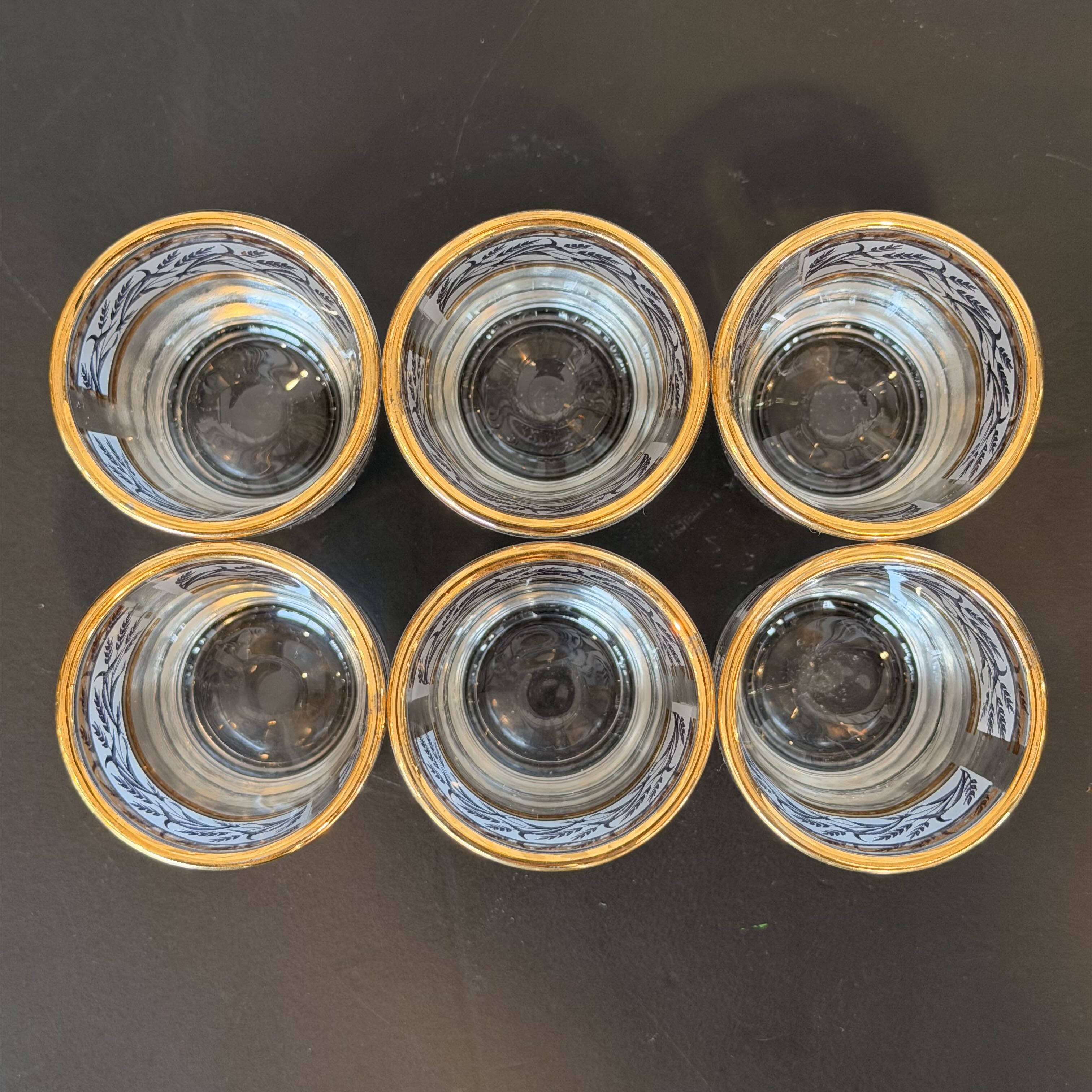 Six clear glass tumblers with gold rims on a dark surface