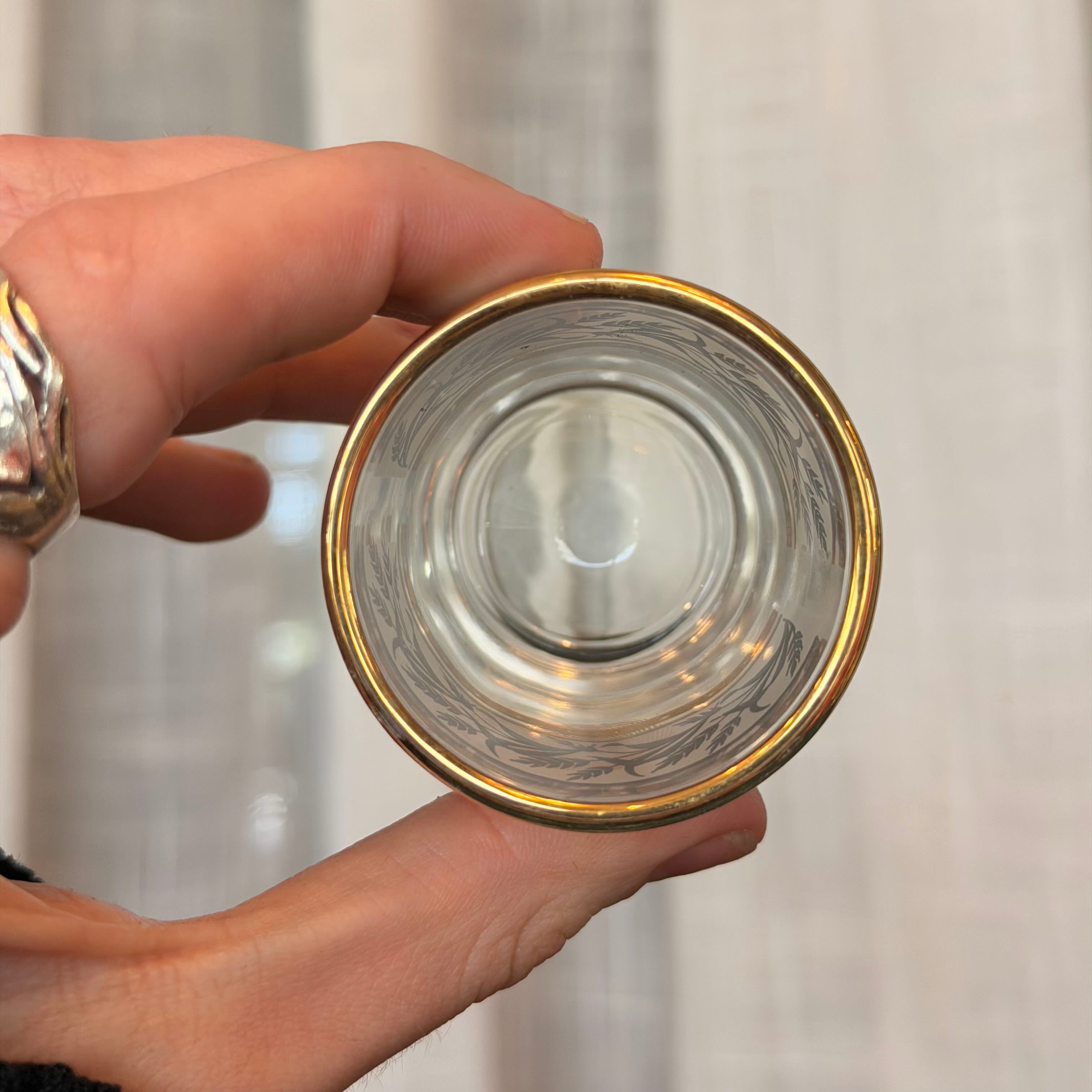 Clear glass with gold rim held by a hand against a neutral background