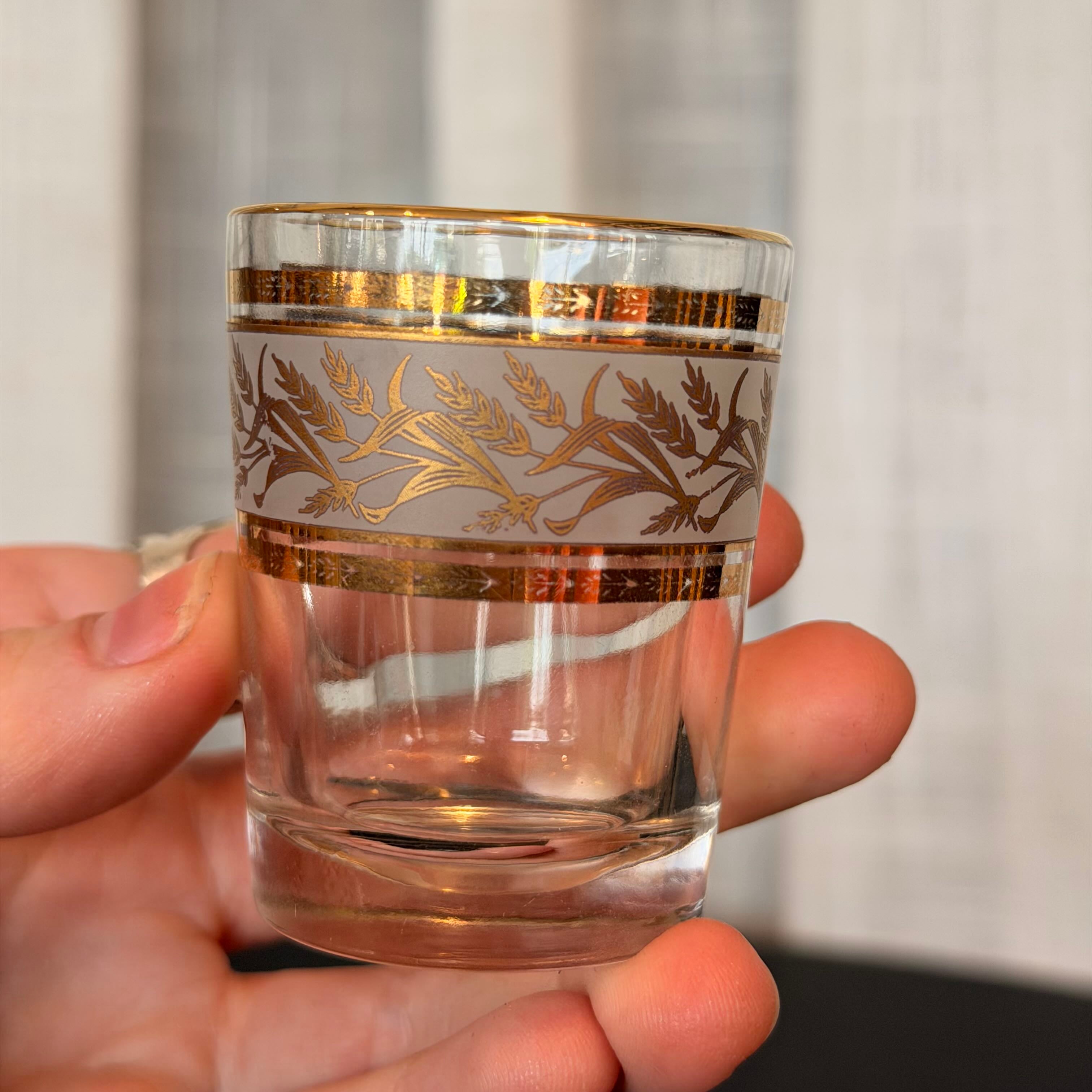 Clear glass with gold decorative patterns held in a hand against a neutral background