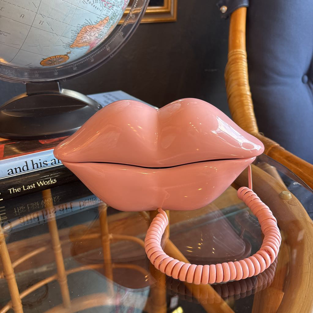 A corded phone of pink lips on a glass table in a room setting.