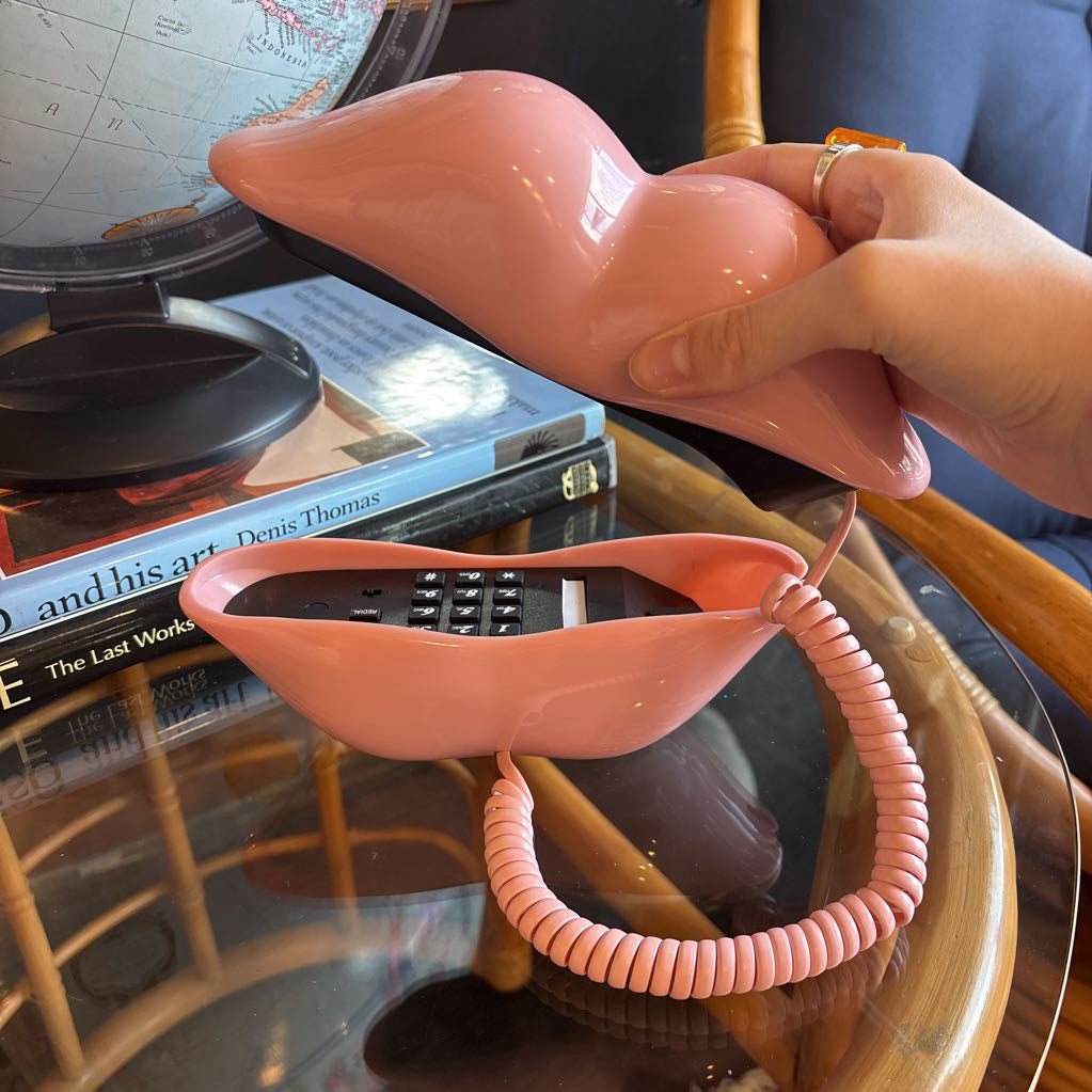 A corded phone of pink lips on a glass table in a room setting.