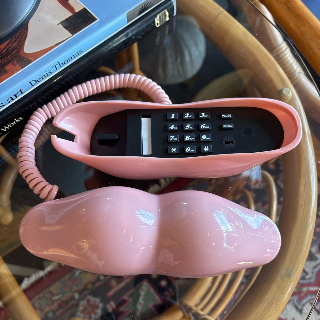 A corded phone of pink lips on a glass table in a room setting.