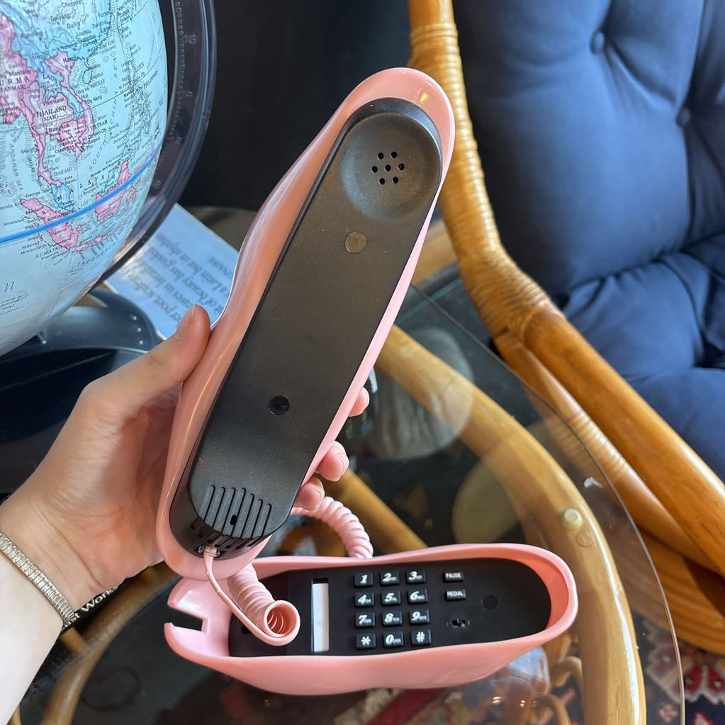 A corded phone of pink lips on a glass table in a room setting.