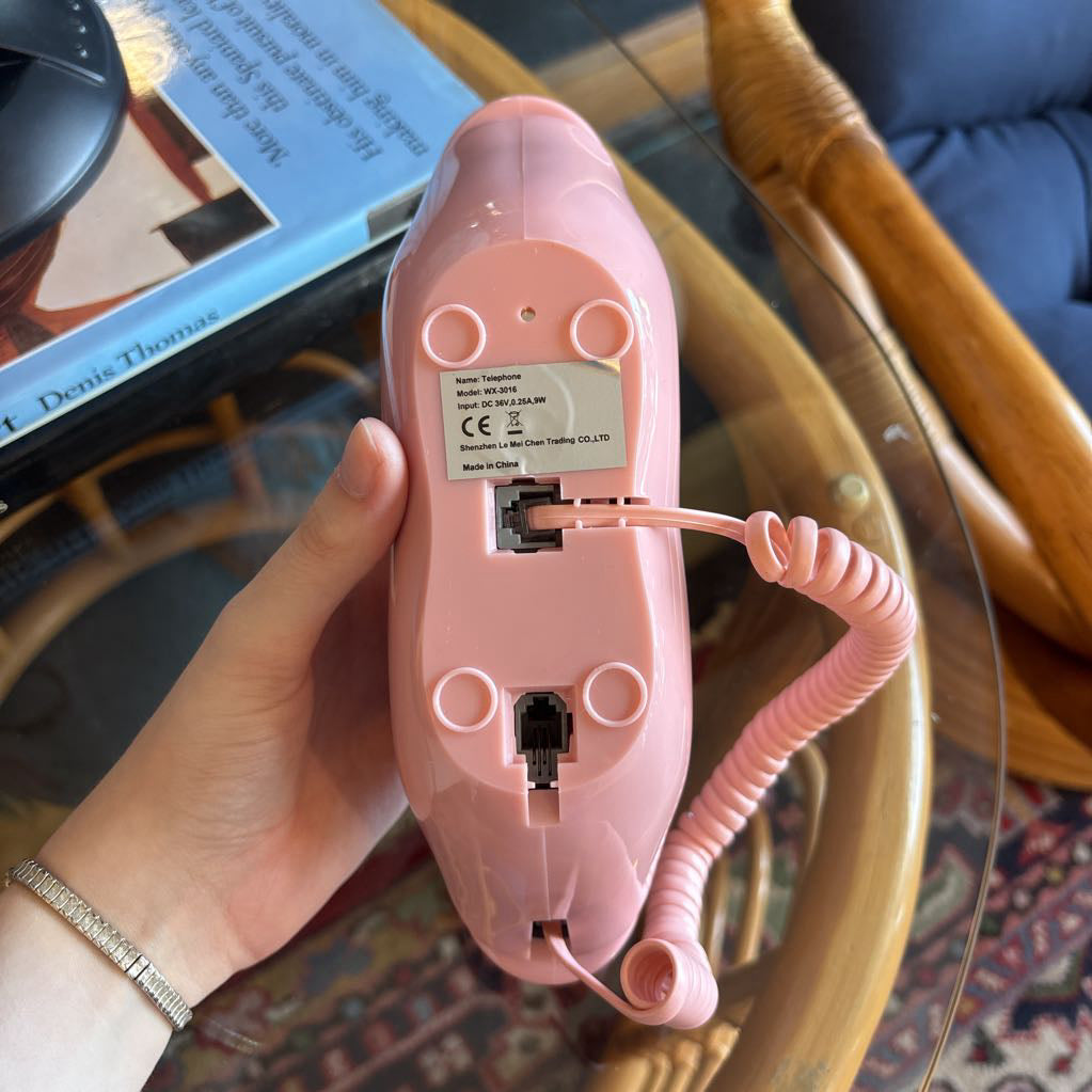 A corded phone of pink lips on a glass table in a room setting.