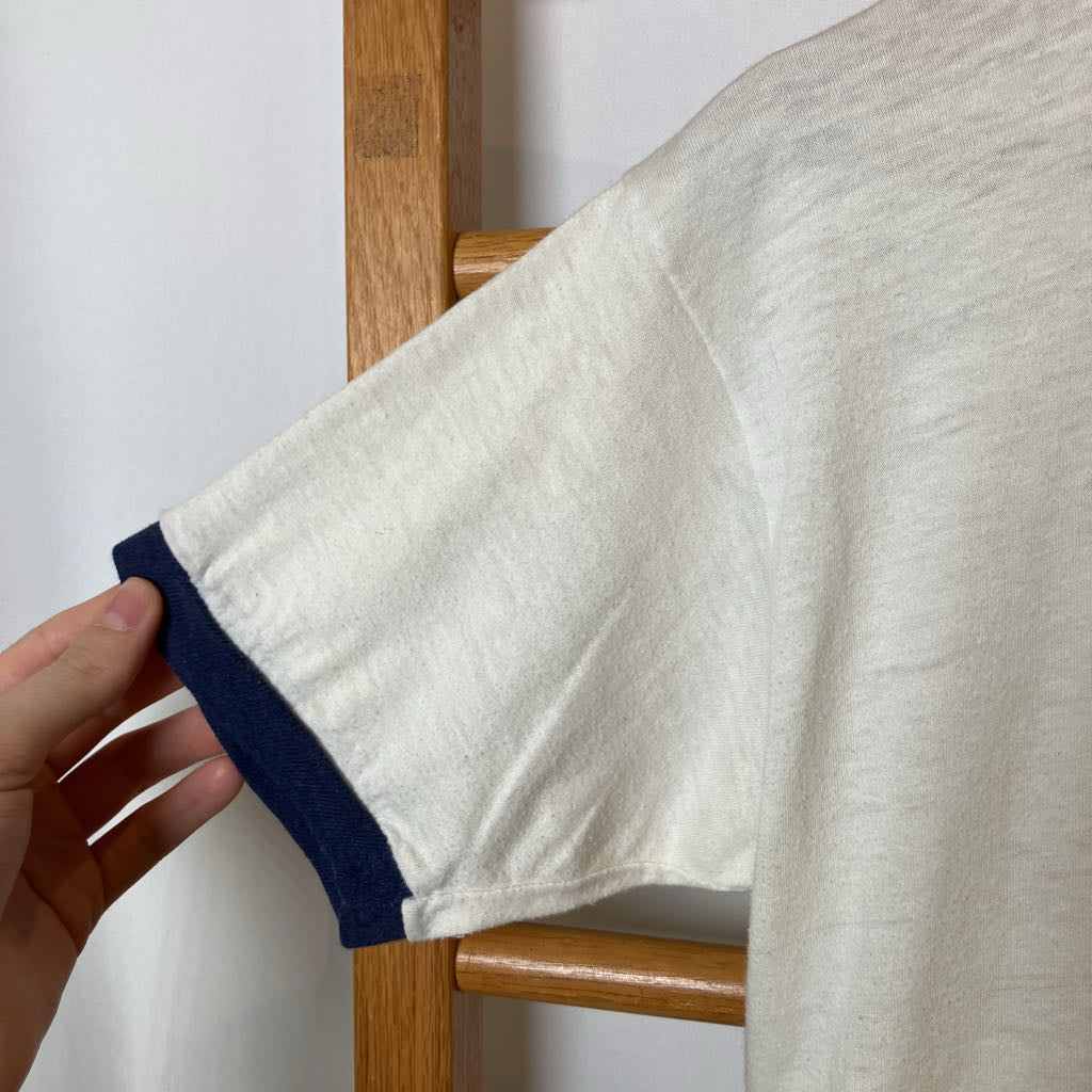 Close-up of a white fabric with blue trim being held by a hand against a wooden chair.