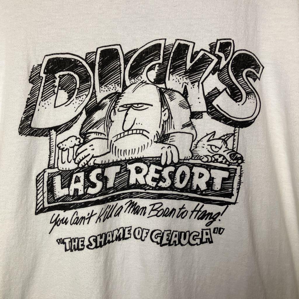 A close-up of a white graphic t-shirt featuring a black hand-drawn style illustration of a man with a beard and the text 'DICK'S LAST RESORT' and 'You Can't Kill a Man Born to Hang! "THE SHAME OF GEAUGA"'.