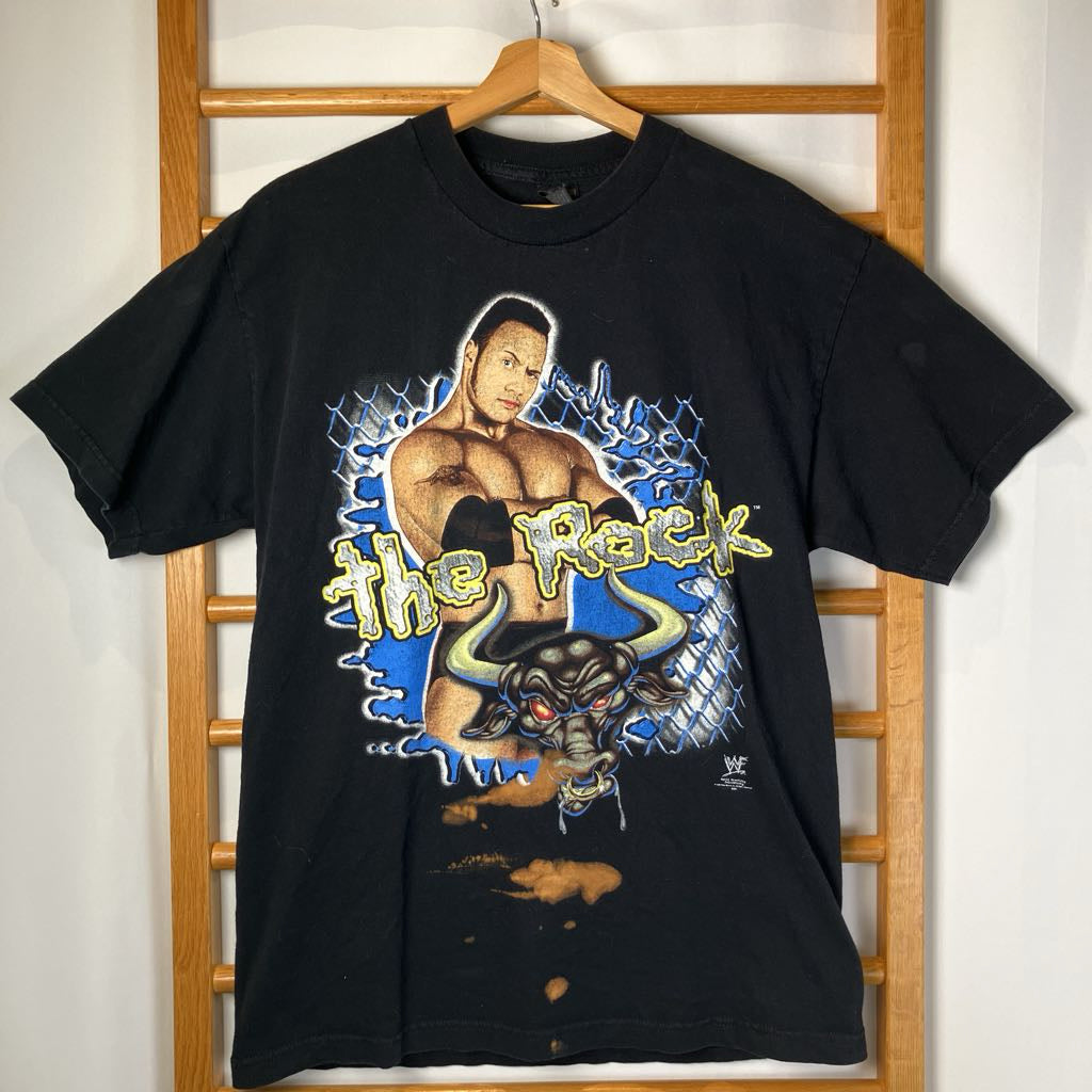 Black t-shirt with 'The Rock' graphic design on a wooden hanger against a white wall.