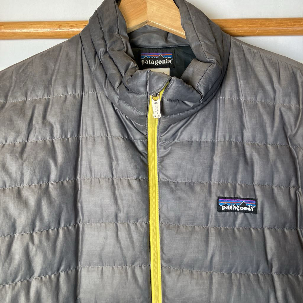 Gray puffer jacket with yellow zipper on a hanger, featuring Patagonia branding.
