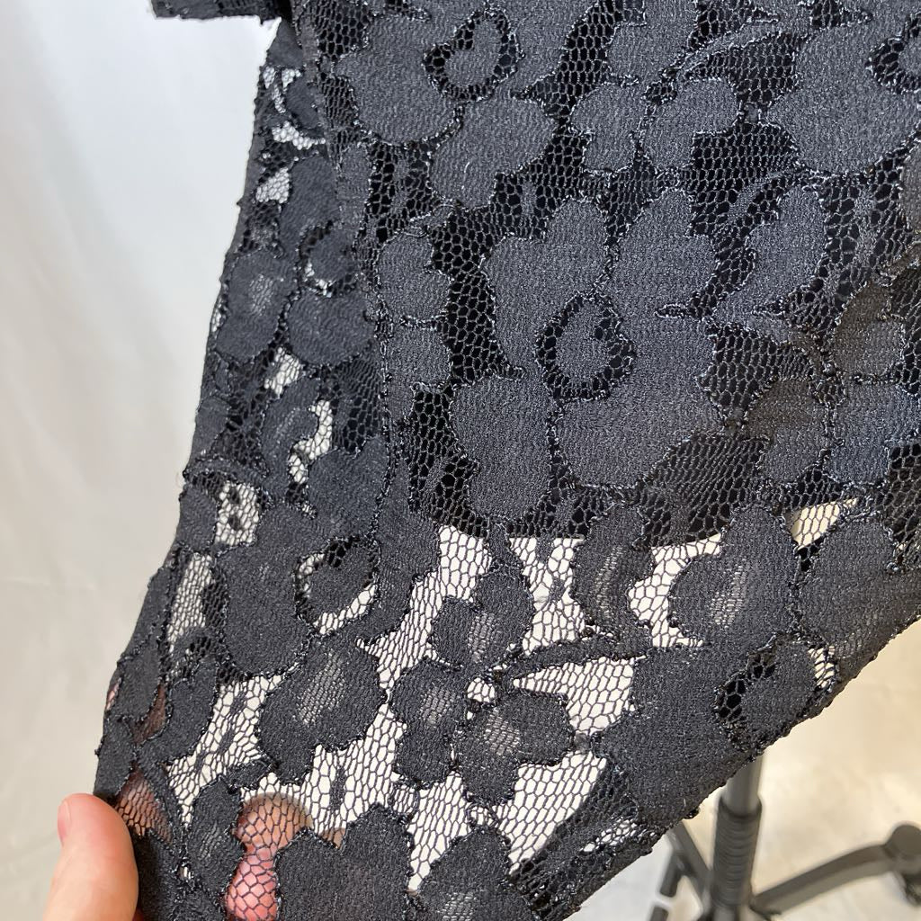 Close-up of black floral lace fabric held by a hand against a neutral background