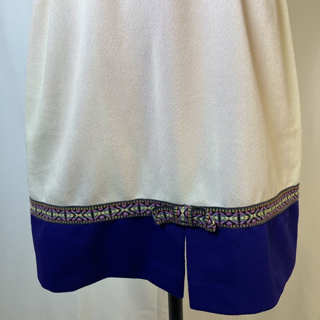 White garment with blue bottom and decorative trim on a mannequin against a plain background