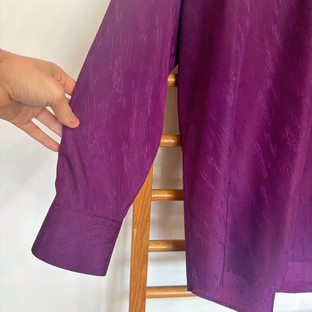 Purple fabric draped over a wooden chair with a hand holding it.