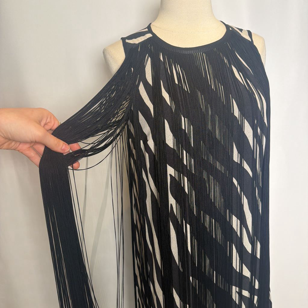 Zebra print dress with a hand holding black fringe on a mannequin in front of a white wall. 
