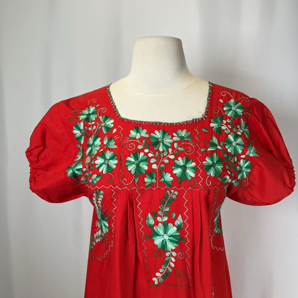 Red blouse with green floral embroidery on a mannequin against a white background