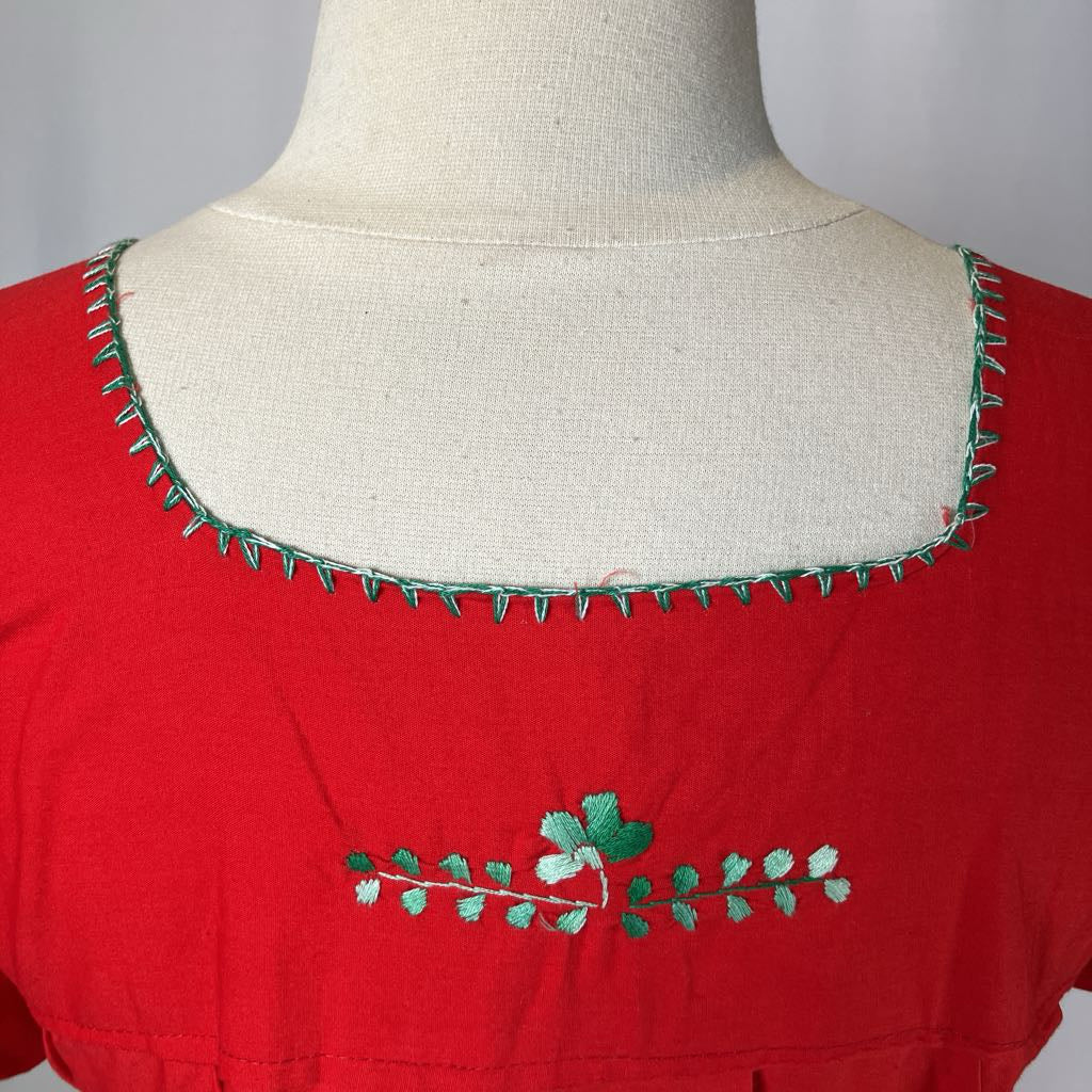 Red blouse with green embroidery on a mannequin against a gray background