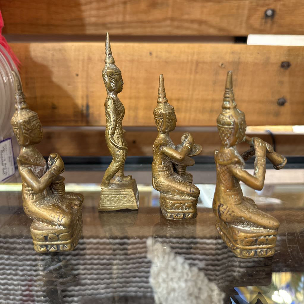 Set of four gold-colored statues on a reflective surface with a wooden background