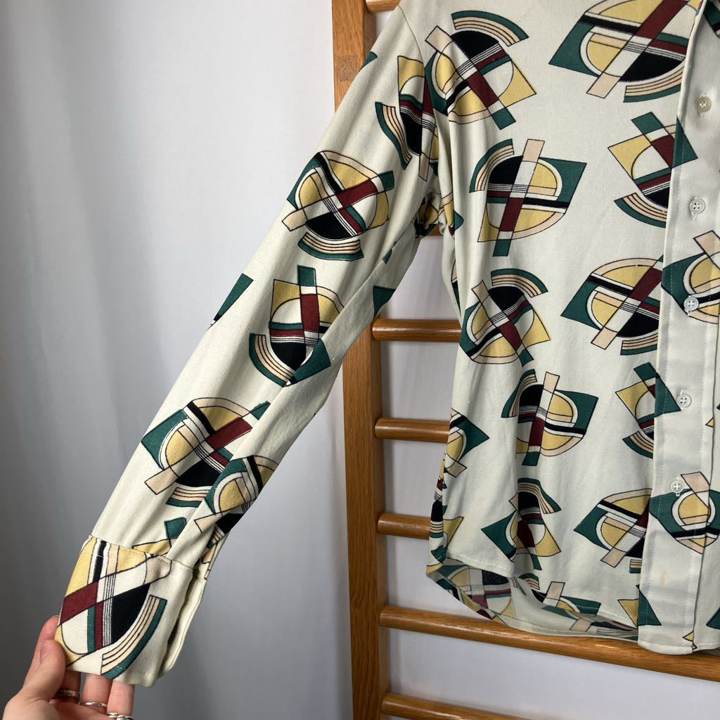 Shirt with geometric pattern hanging on a wooden rack against a gray wall