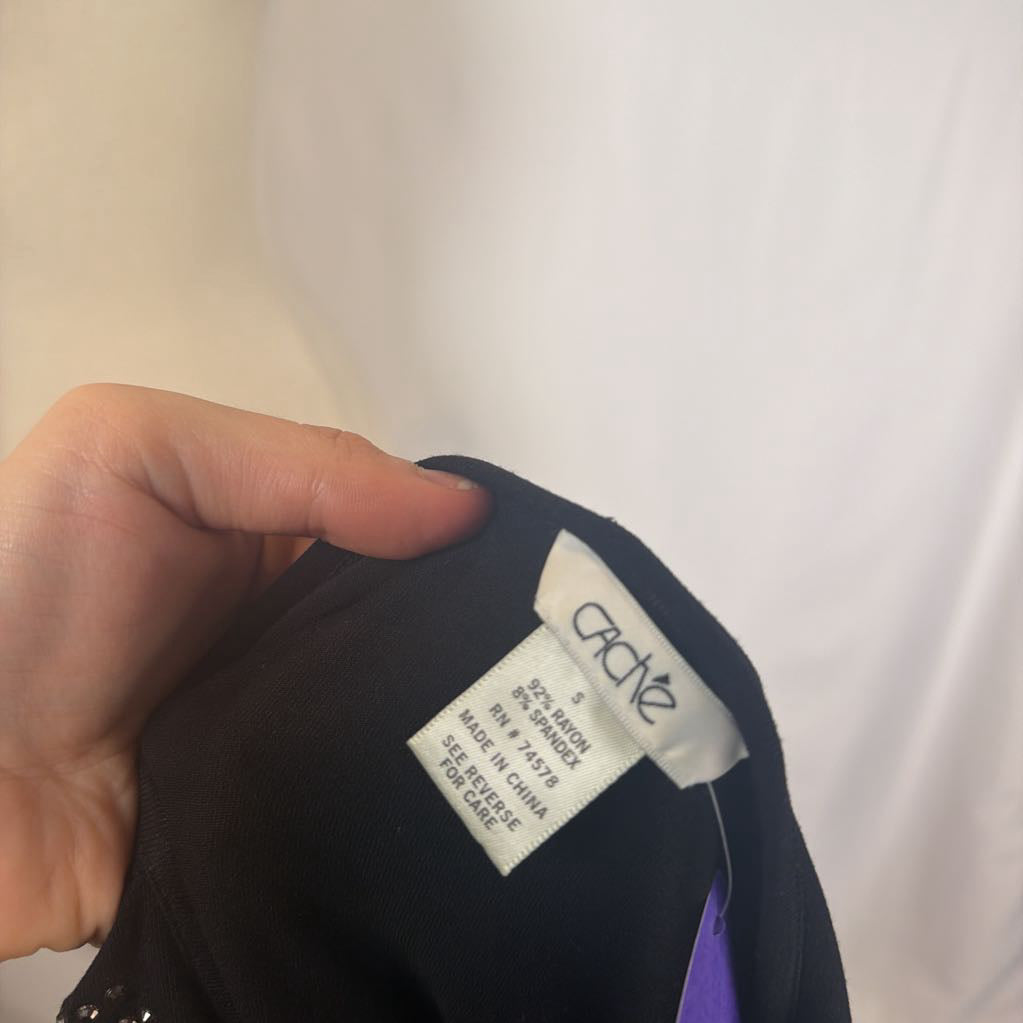 A hand holding a tag with the brand Cache. 